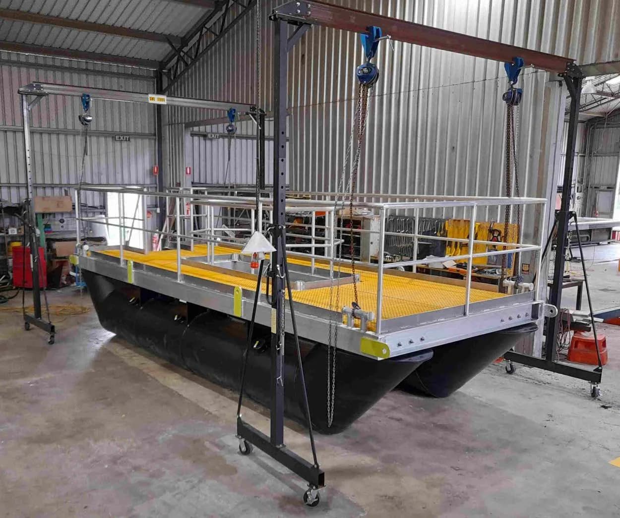 Modular HDPE barge with yellow deck and handrails under a gantry crane in the workshop