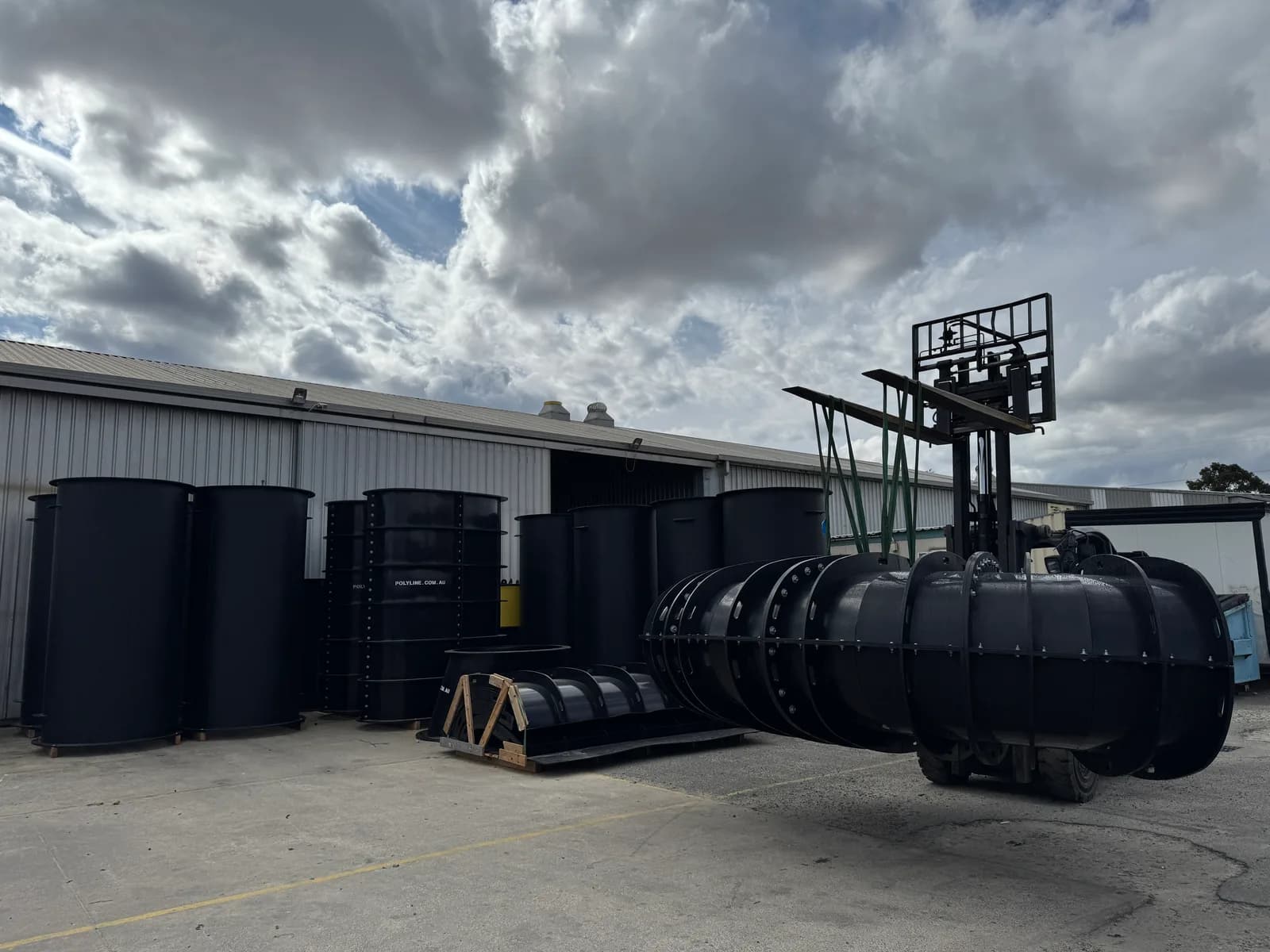 Segmented ducting on a forklift beside fabricated HDPE tanks in the yard
